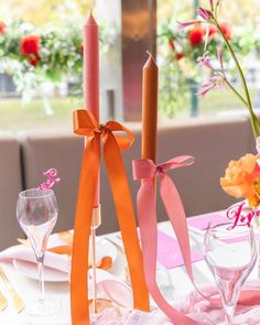 the table is set with pink and orange flowers in vases, candles, and napkins