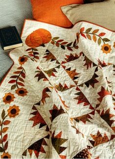 an orange and white quilt sitting on top of a bed next to a pillow with a book