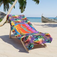 a colorful beach towel is laying on the sand next to a boat and palm trees