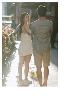 a man and woman walking down the street in front of some flower boxes with flowers on them