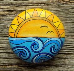 a painted rock sitting on top of a wooden table next to a tree trunk with the sun and ocean waves painted on it