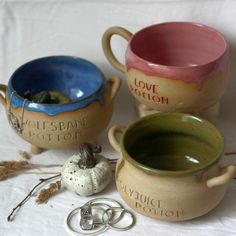 three ceramic mugs sitting next to each other on a white cloth covered tablecloth