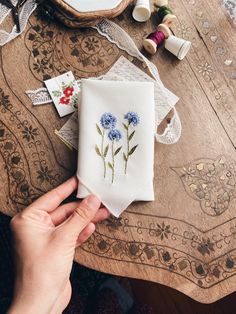 a person is holding a piece of cloth with blue flowers on it and sewing thread