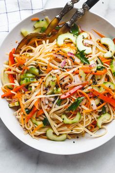 a white bowl filled with noodles and veggies on top of a marble table