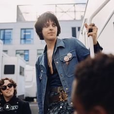 a man with sunglasses and a denim jacket is standing on the street next to other people