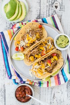 three tacos on a plate with guacamole and salsa