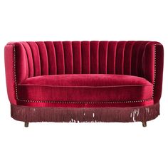 a red velvet sofa with fringe trimmings and studded detailing on the legs