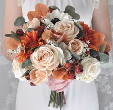 a bride holding a bouquet of white and orange flowers on her wedding day in front of a wall