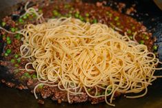 some noodles are being cooked in a wok with meat and peas on the side