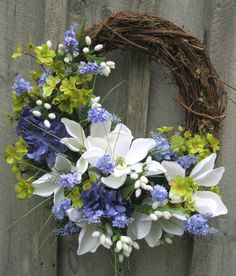 a wreath with white and blue flowers is hanging on a fence