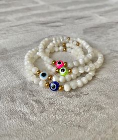 💕Evil Eye Bracelets, handcrafted from stunning 100% natural mother of pearl shell and high quality gold tarnish resistant beads💕 The evil eye is a protective and powerful symbol, also known as the Nazar. The evil eye helps to absorb negative energies, protect and bring luck. The evil eye makes a perfect gift for yourself and loved ones.  ✨All bracelets are lovingly handmade by me using high quality materials✨ Hand of Fatima Necklace https://www.etsy.com/uk/listing/1556603231/hamsa-hand-of-fatima-gold-pendant?click_key=a6f5da90d8d8ea8bd774c20becf761f1cd89bc53%3A1556603231&click_sum=a9a084e9&ref=shop_home_active_3 Hand of Fatima Earrings https://www.etsy.com/uk/listing/1542499652/hamsa-hand-of-fatima-gold-stud-earrings?click_key=89cabcb8ef68040716616f6d3e33732975d65ab1%3A1542499652&click_s Mother Of Pearl Beaded Bracelet As A Gift, Adjustable Mother Of Pearl Bracelets As Gifts, Adjustable Mother Of Pearl Bracelets For Gifts, Adjustable Mother Of Pearl Bracelet As Gift, Spiritual White Beaded Bracelets With Evil Eye, White Evil Eye Beaded Bracelets, White Evil Eye Bracelets As Gift, White Beaded Round Evil Eye Bracelet, White Hand-strung Evil Eye Bracelet With Round Beads