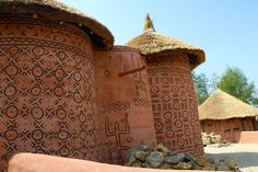 several clay pots with designs on them and grass roof tops in front of some trees