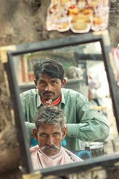 a man is getting his hair cut in front of a mirror with the reflection of another man