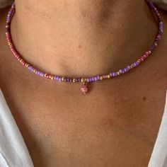 a woman wearing a pink and purple beaded necklace with a heart charm on it