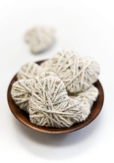 three balls of yarn sit in a bowl on a white surface next to two smaller balls of yarn