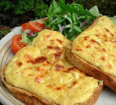 two pieces of bread with cheese on top and salad in the background, sitting on a plate