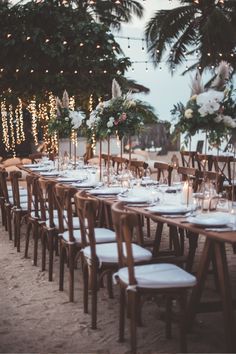 a long table set up with candles, flowers and greenery for an outdoor dinner