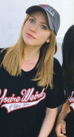 two young women wearing black shirts and baseball caps, one with blonde hair looking at the camera