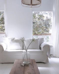 a living room with a white couch, coffee table and two vases on it