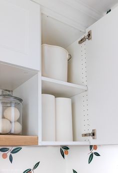 an open cabinet with some white containers and paper towels on the shelf next to it