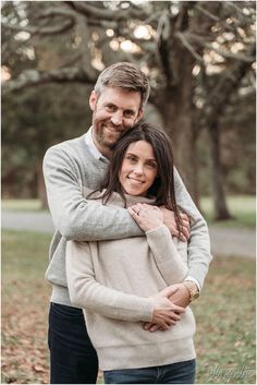 a man and woman hugging each other in front of trees