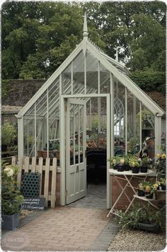 a white greenhouse with lots of plants in the room and on the outside, there is a brick walkway leading up to it