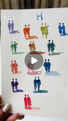 a person holding up a piece of paper with people painted on it in different colors