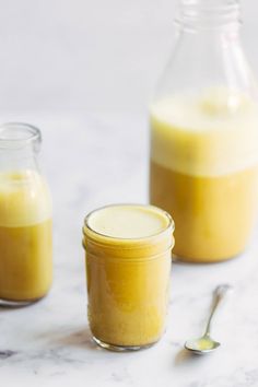 two jars filled with liquid sitting on top of a white counter next to spoons