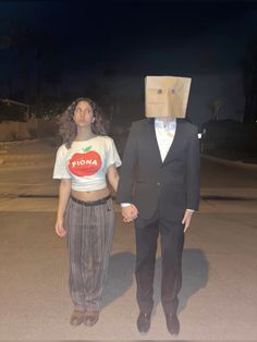 a man and woman wearing paper bags on their heads walking down the street at night