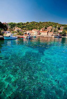 the water is crystal blue and clear with small boats in it's coves