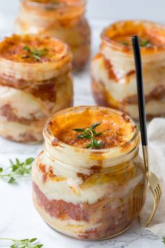 four jars filled with food sitting on top of a white table next to a fork