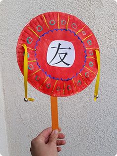 a hand holding up a paper plate with chinese writing on it and an orange stick