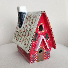 a red birdhouse with decorative decorations on it's roof sits on a white surface