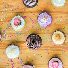 many cupcakes are arranged on a wooden table with sprinkles and frosting