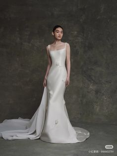 a woman in a white wedding dress standing next to a gray wall and posing for the camera