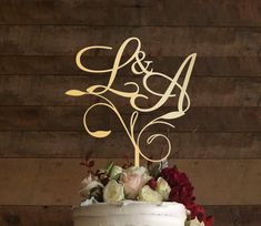 a wedding cake with the initials on it and flowers in front of a wooden wall