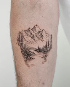 a man with a tattoo on his leg that has mountains and trees in the background