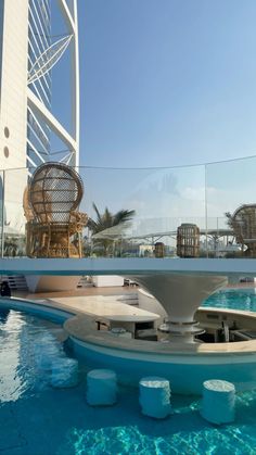 an outdoor swimming pool with chairs and tables in the water near a tall white building