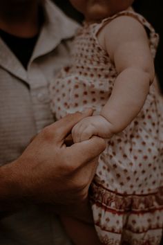 a man holding a small baby in his arms while he holds the hand of it's mother