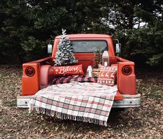 an old red pickup truck with christmas decorations on the bed and plaid tablecloth in the back