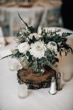 a vase filled with white flowers sitting on top of a wooden table next to candles