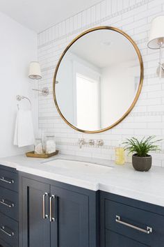 a bathroom vanity with a round mirror above it and a plant on the counter top