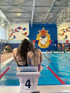 two women are sitting at the edge of a swimming pool and watching another woman swim