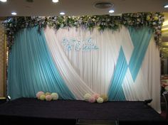 the backdrop is decorated with blue and white draping, flowers and greenery