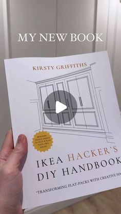 a person holding up a book about ikea hackers diy handbook in front of a door