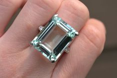 1920's cocktail ring with emerald cut aquamarine stone. 18.43 Carat aquamarine with six 0.18 carat diamonds on a 14kt white gold band. Aquamarine clarity A-AA and is 19.7mm x 15.2mm. Metal weight is 10.0g. Appraised value is $10,940 as of 08/09/2022. Appraisal paperwork available upon request. Please feel free to reach out with any questions! Formal Emerald Cut Aquamarine Diamond Ring, Formal Emerald-cut Aquamarine Diamond Ring, Formal Aquamarine Ring With Emerald Cut, Formal Emerald-cut Aquamarine Ring, Formal Emerald Cut Aquamarine Ring, Formal Rectangular Aquamarine Rings, Aquamarine Cocktail Ring, Swarovski Ring, Lapis Ring