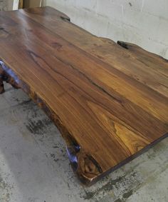 a large wooden table sitting on top of a cement floor next to a white brick wall