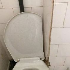 a white toilet sitting in a bathroom next to a wall with peeling paint on it