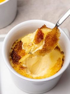 a spoon with some food in it on a white plate next to two mugs