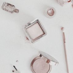 various cosmetics and makeup products on a white surface with scattered powder, eye shadow, lip balm, brush